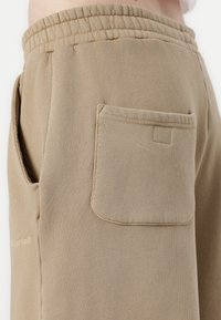 Beżowe dresy wykonane z miękkiej mieszanki bawełny, z elastycznym paskiem w talii, bocznymi kieszeniami oraz jedną tylną kieszenią z przeszyciami.