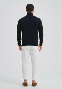 Pull à col roulé en tricot navy associé à un pantalon blanc. Coupe ajustée, poignets et col côtelés, texture douce. Chaussures à enfiler marron.