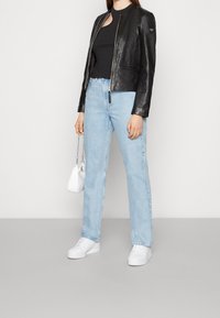 Svart läderjacka, svart topp, ljusblå raka jeans, vita sneakers, håller en liten vit väska med kedja.