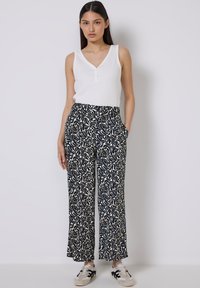 Witte mouwloze top met een V-hals, gecombineerd met ruime marineblauwe broek met een crèmekleurig bloemenpatroon en zijzakken. Sneakers maken de outfit compleet.