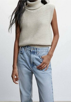 Pull en maille à col roulé beige clair, motif texturé, associé à un jean en denim bleu clair taille haute.