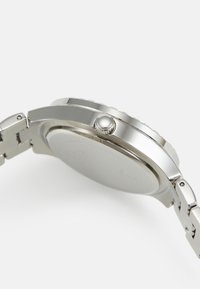 Zilveren metalen horloge met een ronde kast, gestructureerde bezel en een gepolijste kroon. De band heeft geschakelde metalen segmenten die het licht weerkaatsen.