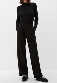 Black long-sleeve top with a high neckline, paired with high-waisted, wide-leg black trousers. Black platform shoes with metallic accents.