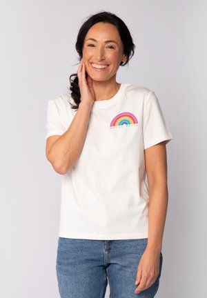 Witte katoenen t-shirt met een kleurrijk regenboogontwerp en de tekst "VROUWEN KRAACHT" in het blauw, gecombineerd met een blauwe spijkerbroek.