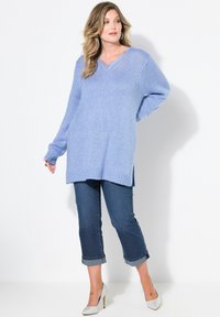 Světle modrý pletený svetr s výstřihem do V, dlouhými rukávy a bočními rozparky, v kombinaci se zkrácenými džínami a stříbrnými vysokými podpatky.