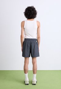 Grå atletikshorts med elastisk talje og sidelomme, parret med en hvid tanktop og hvide ankelstrømper. Baggrunden er lys.