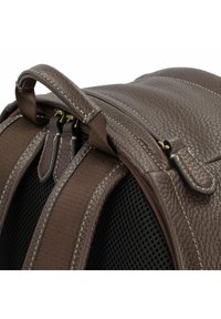 Sac à dos en cuir marron avec surface texturée, doubles zips, bretelles en tissu et panneau arrière en maille pour la ventilation.