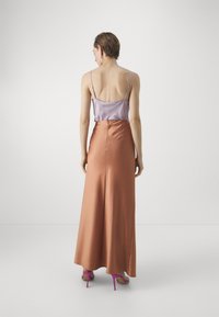 Top in satin lavanda con spalline regolabili abbinato a una gonna maxi fluida in satin color ruggine, completato da sandali con tacco alti rosa.