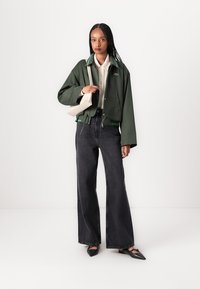 Groene cropped jas met witte accenten en elastische zoom, gecombineerd met hoge zwarte wijde pijpen spijkerbroek en zwarte puntige flats.
