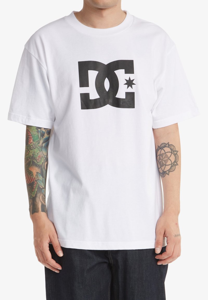 Weißes Baumwoll-T-Shirt mit einem großen schwarzen Drucklogo von DC und einem Sternakzent. Kurze Ärmel und eine entspannte Passform.