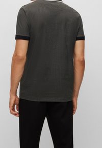 Polo a maniche corte di colore nero con un motivo testurizzato, colletto bianco e dettagli neri sulle maniche, realizzato in un materiale leggero.