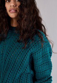 Maglione in maglia teal caratterizzato da un motivo testurizzato con dettagli ad a riff. Ha un collo tondo e maniche lunghe con bordi a coste.