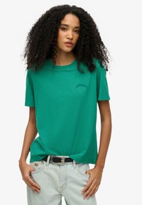 Groene crewneck t-shirt van zachte stof, met een klein geborduurd "Superdry" logo. Gecombineerd met lichtblauwe denim jeans en een zwarte riem.