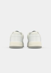 Par tenisica u bijeloj boji s bež srednjim svojim dijelom i sivim vanjskim dijelom prikazanih sa stražnje strane na bijeloj pozadini.