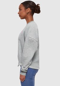 Grijze fleece sweatshirt met een ronde hals en oversized mouwen. Beschikt over een koord onderaan en een klein roze ontwerp op de voorkant.