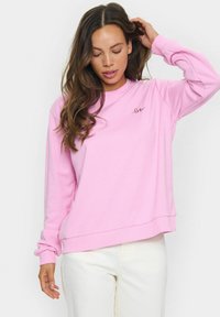 Svetlo roza crewneck dukserica, izdelana iz mehke tkanine z rebrastimi manšetami. Na prsih ima majhen črni vezeni dizajn z napisom 'love'.