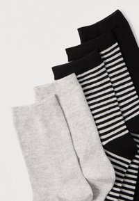 Quatre paires de chaussettes : deux unies en gris et noir, une noire avec des rayures blanches, et une autre totalement noire. Toutes ont des bords côtelés et une texture douce.