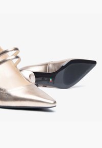 Scarpe con tacchi alti color oro metallico con punta affilata, dotate di tre fasce decorative e una suola nera testurizzata. Fatto in Italia.