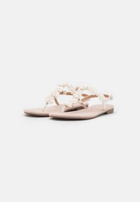 White floral thong sandals with soft, textured insole and a flat heel. The floral accents are placed along the straps for decoration.