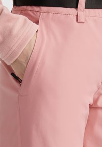 Pink outdoor pants made of smooth fabric, featuring a side pocket with a zipper and a black waistband. Slightly tapered design.