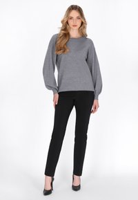 Grauer Pullover mit Ballonärmeln, kombiniert mit schwarzen Slim-Fit-Hosen und schwarzen High Heels, vor einem neutralen Hintergrund.