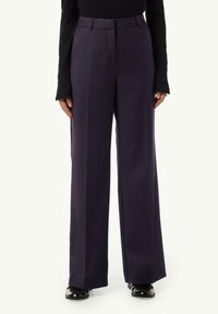 Wide-leg trousers in deep navy with a smooth fabric, featuring a high waist, front pleats, and side pockets. Glossy black shoes complete the look.