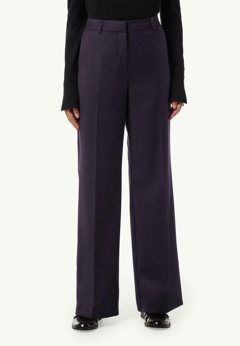 Wide-leg trousers in deep navy with a smooth fabric, featuring a high waist, front pleats, and side pockets. Glossy black shoes complete the look.