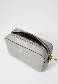 Grå läder kosmetikväska med en slät yta, rektangulär form, guld blixtlås och en guld logotyp på framsidan. Blixtlåsets öppning upptill.