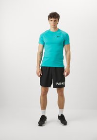 Türkisfarbendes Sport-T-Shirt, schwarze Shorts mit weißem "NIKE"-Schriftzug, strukturierter Stoff, Sneaker und weiße Sportsocken.
