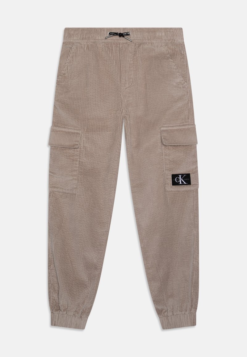 Beige corduroy cargo pants with elastic cuffs, two side pockets, and a patch logo. Features a drawstring waistband and textured fabric.