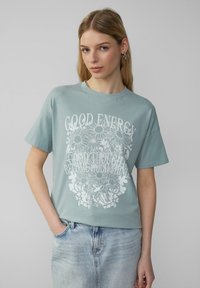Mintgroene oversized t-shirt van katoen, met een witte grafische print met bloemenontwerp en tekst, korte mouwen en ronde halslijn.