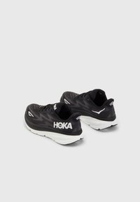 Scarpe da corsa nere con un motivo testurizzato, dettagli bianchi e una suola spessa bianca. Logo HOKA ben visibile sul lato.