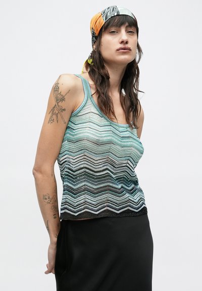 Αμάνικο τοπ με μοτίβο ζιγκ-ζαγκ σε ανοιχτό μπλε και μαύρο, με γυαλιστερή υφή. Οι τιράντες είναι λεπτές και το τελείωμα έχει διακριτικές μεταλλικές λεπτομέρειες.