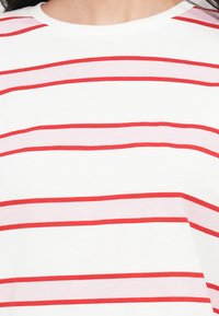 Ριγέ μπλουζάκι σε λευκό με κόκκινες και ανοιχτό ροζ οριζόντιες ρίγες· διαθέτει στρογγυλή λαιμόκοψη και απαλό, ελαφρύ ύφασμα.