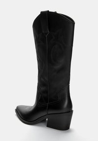Zwarte leren cowboylaars met een spitse neus, decoratieve stiksels en een blokhak van gemiddelde hoogte. Heeft een trekband aan de bovenkant.