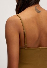 Olivgrünes, geripptes Oberteil mit verstellbaren Trägern, glatter Textur und Rückendesign mit tiefem Ausschnitt, das ein sichtbares Tattoo nahe der Schulter zeigt.