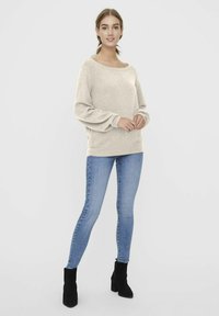 Pull en tricot beige avec un encolure dégagée et des manches ballon, associé à un jean skinny bleu clair et des bottines noires.