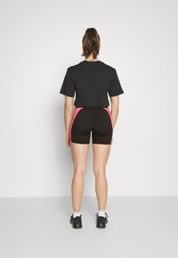 Svart t-shirt med korta ärmar, kombinerad med svarta shorts med rosa sidopaneler. Bärs med svarta sneakers och vita ankelsockor.