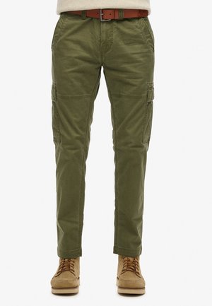Pantaloni cargo verde oliva con molte tasche, design aderente e una texture liscia. Abbinati a scarpe beige con lacci e una cintura marrone.