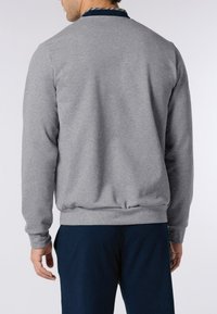 Uomo che indossa un pullover grigio chiaro a maniche lunghe con una vita a coste e pantaloni blu scuro, visto da dietro.