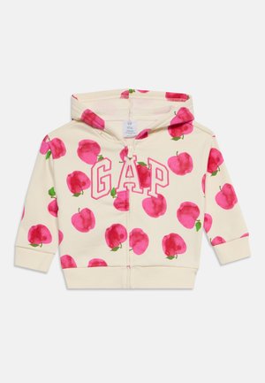 Sweat à capuche pour enfants couleur crème avec des imprimés de pommes roses et de grandes lettres GAP roses en contour sur le devant, avec une fermeture éclair sur le devant et une capuche.