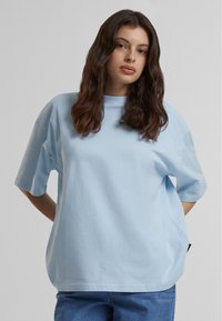 Camiseta de algodón de gran tamaño en azul claro, con mangas cortas, cuello redondo y un sutil detalle de logo en el frente. Ajuste suave y relajado.