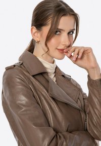 Braune Leder-Motorradjacke mit breitem Kragen, Reißverschluss vorne und Schulterklappen. Das Modell zeigt einen dezenten Glanz und eine strukturierte Oberfläche.