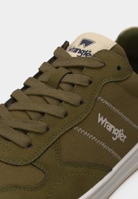 Oliiviroheline Wrangler tennisejäts kangast ja seemisnahast paneelidega, tekstuursete nööride, valge siksakõmbluse ning külje- ja keeleosale paigaldatud brändiloogoga.