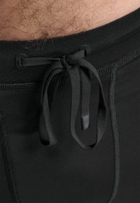 Sorte atletiske shorts med snørrelukning i taljen. Stoffet er glat og strækbart, med flade sømme langs sømmene.