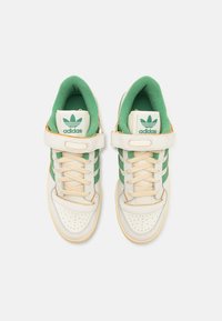 Sneaker Adidas bianchi e verdi con collare imbottito, fascia a velo e punta perforata. Presenta strisce verdi e una suola testurizzata.