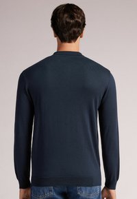 Granatowy sweter w dzianinę z długimi rękawami, okrągłym dekoltem i gładką fakturą; posiada prążkowany dół i mankiety.