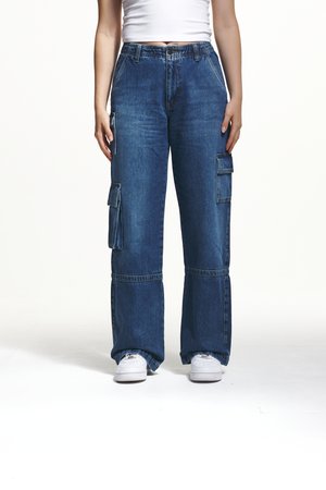 Pantalons cargo en denim bleu amples avec une taille haute, comportant de grandes poches latérales, une coupe décontractée et une jambe droite. Associés à des baskets blanches.