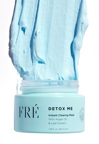 Jasnoniebieski okrągły słoik z przezroczystą pokrywką, etykieta produktu głosi "DETOX ME Maskę Natychmiastowo Oczyszczającą", w środku znajduje się gęsta niebieska kremowa substancja wypływająca na zewnątrz.