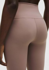 Colanți cu talie înaltă dintr-un material moale de culoare roz pal. Textură netedă cu cusături minime, concepuți pentru confort și elasticitate.